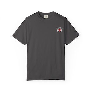 May include: Dark gray t-shirt with a small red wolf logo and the words "LIFT FOR MORE" printed on the upper right chest. The shirt is a short-sleeved, crew neck style.