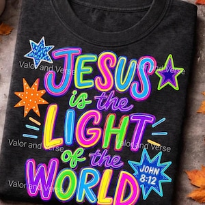 May include: A charcoal gray t-shirt featuring the colorful text "JESUS is the LIGHT of the WORLD" and "JOHN 8:12" inside a blue star. The design includes neon-colored lettering in pink, blue, yellow, and green, accented by various star shapes.