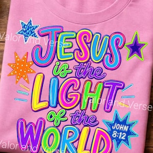 May include: A light pink t-shirt featuring a colorful graphic with the text "JESUS is the LIGHT of the WORLD" and "JOHN 8:12". The design includes various multi-colored stars in blue, orange, and purple, with bright lettering in yellow, pink, blue, and green.