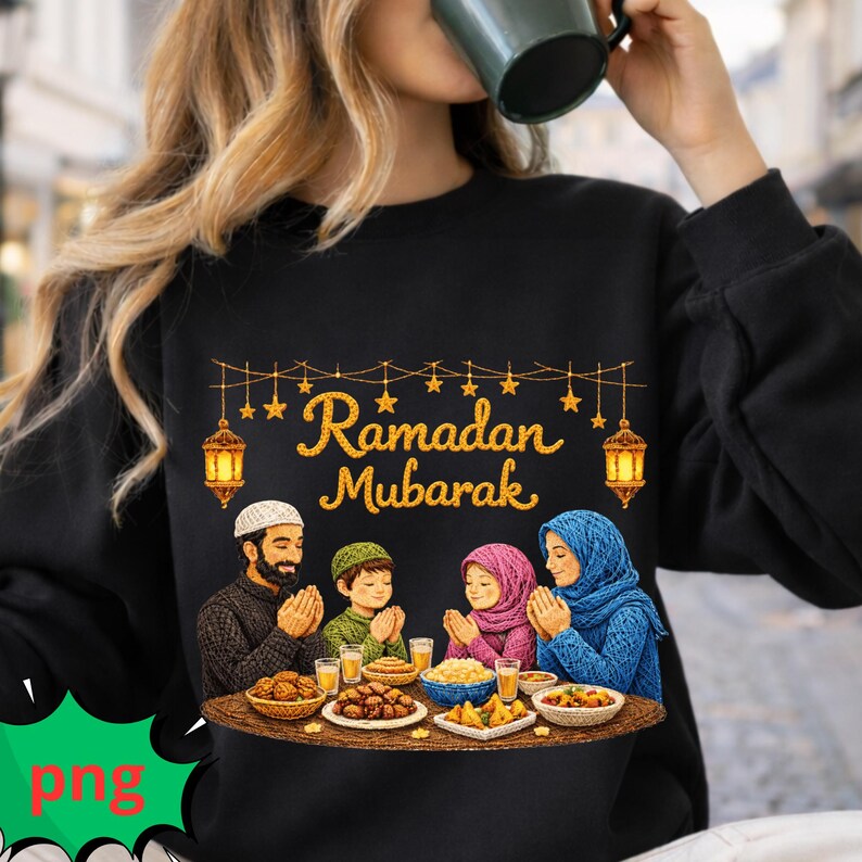 May include: Black sweatshirt featuring a family celebrating Ramadan. The design includes the text "Ramadan Mubarak", lanterns, and a family praying at a table with food. The family members are wearing traditional head coverings. The image is colorful.
