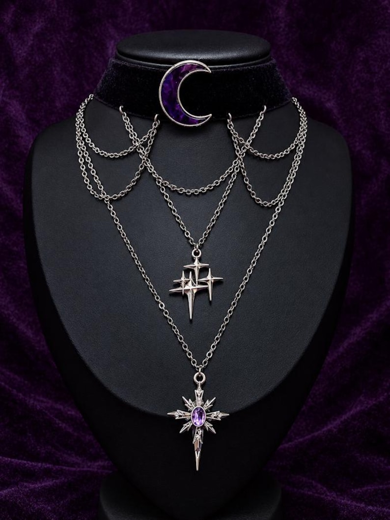 May include: A black velvet choker necklace featuring a purple crescent moon charm, layered silver-tone chains, a cluster of four-pointed star charms, and a central star-shaped pendant with a small purple oval gemstone in the center.