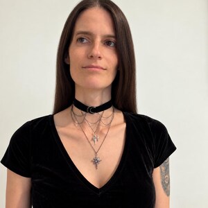 May include: A black velvet choker necklace featuring a silver-toned crescent moon charm at the center. Attached to the choker are multiple delicate silver-toned chains that drape downwards, ending in two distinct star-shaped pendants with small crystals.