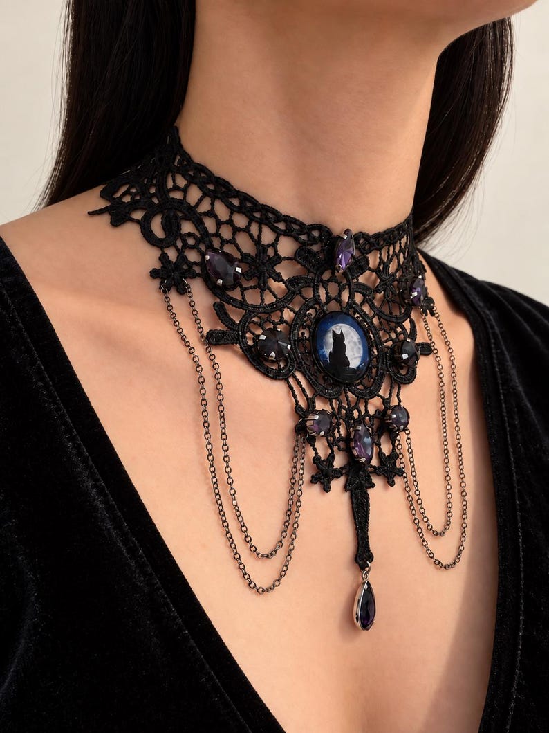 Op de afbeelding: Een zwarte kanten choker ketting met een centrale ovale cabochon met het silhouet van een kat tegen een volle maan. Het sieraad is versierd met donkerpaarse gefacetteerde kristallen en fijne hangende metalen kettinkjes met een druppelhanger.