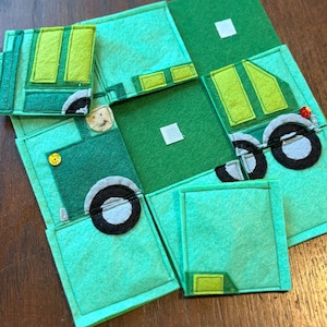May include: A handmade felt toy featuring a green and light green truck design. The toy is composed of several squares and rectangles, with details like wheels, windows, and a button. The toy is designed for children.
