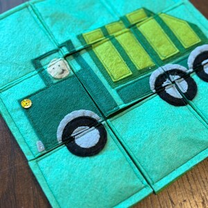 Pu&ograve; includere: Un puzzle in feltro verde con un design a forma di camion. Il camion &egrave; composto da varie tonalit&agrave; di verde e ha ruote nere e grigie. Un piccolo volto sorridente &egrave; visibile nel sedile del conducente. Il puzzle &egrave; composto da diversi quadrati collegati.