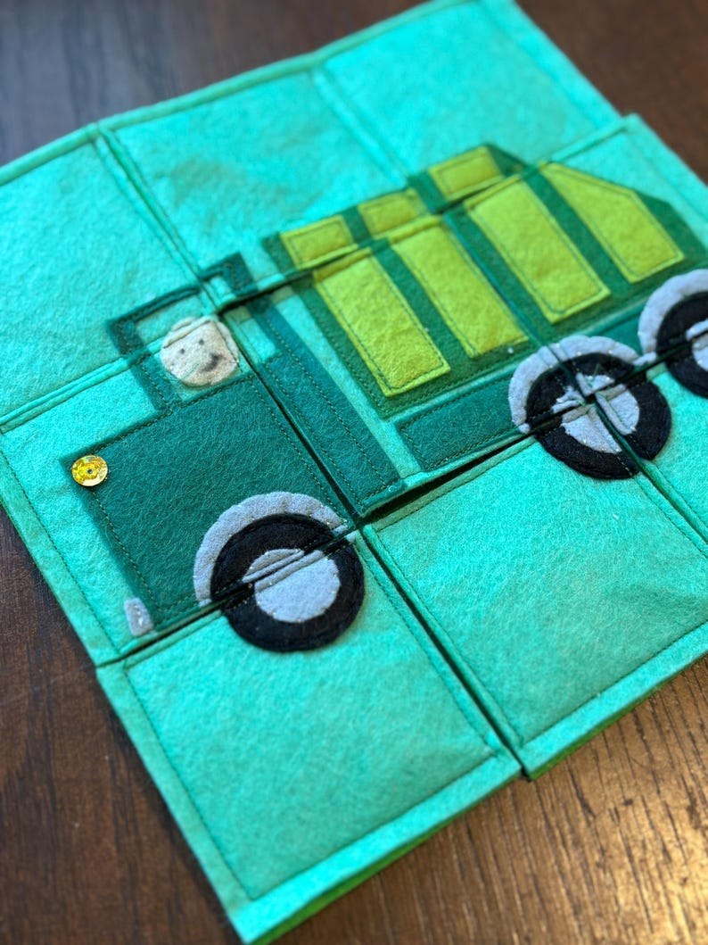 Pu&ograve; includere: Un puzzle in feltro verde con un design a forma di camion. Il camion &egrave; composto da varie tonalit&agrave; di verde e ha ruote nere e grigie. Un piccolo volto sorridente &egrave; visibile nel sedile del conducente. Il puzzle &egrave; composto da diversi quadrati collegati.
