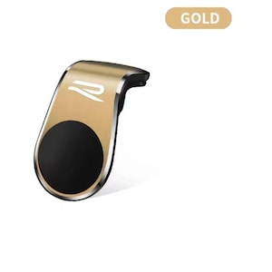 以下が含まれることがあります： 黒い円形の磁気部分を備えた、金色の車の電話マウント。 マウントは湾曲したデザインで、白いロゴが付いています。 「GOLD」という単語は、右上隅にある金色の長方形の中にあります。