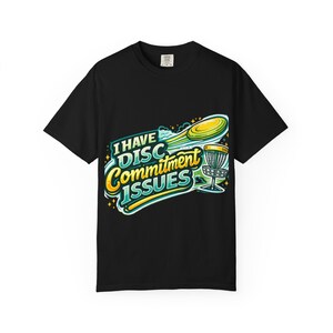 Może przedstawiać: Czarny t-shirt z kolorowym nadrukiem graficznym. Projekt przedstawia dysk i kosz do disc golfa, a także tekst "I HAVE DISC COMMITMENT ISSUES" w zabawnej czcionce. Koszulka wykonana jest z miękkiego materiału.