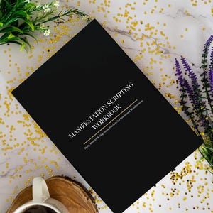 May include: A black workbook titled "Manifestation Scripting Workbook" with gold text, surrounded by white flowers, purple lavender, and gold star-shaped confetti. A white mug of coffee sits on a wooden coaster.