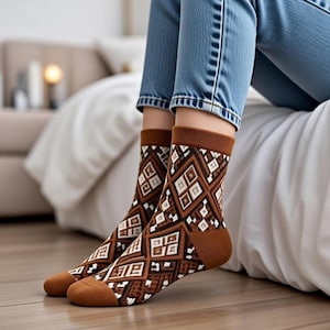 May include: A pair of brown and white patterned socks. The socks have a geometric design with brown heels, toes, and cuffs. The socks are worn with blue jeans. The socks are on a white bed.