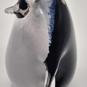 May include: A glass penguin figurine with a rounded body and a clear beak. The penguin's body is primarily white, with black and blue accents on the back and head. The figurine is a decorative item.