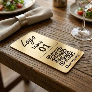 May include: A rectangular gold table sign with the text "Logo", "TABLE 01", and "Our menu". A QR code is also printed on the sign. The sign is on a wooden table, next to a napkin and a wine glass.