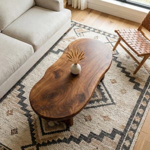 Könnte beinhalten: Wohnzimmer mit einem dunklen Holz-Couchtisch mit organischer Form. Der Teppich zeigt beige, schwarze und braune geometrische Muster. Ein beiges Sofa und ein Lederstuhl ergänzen das Bild. Der Tisch ist etwa 150 cm lang.