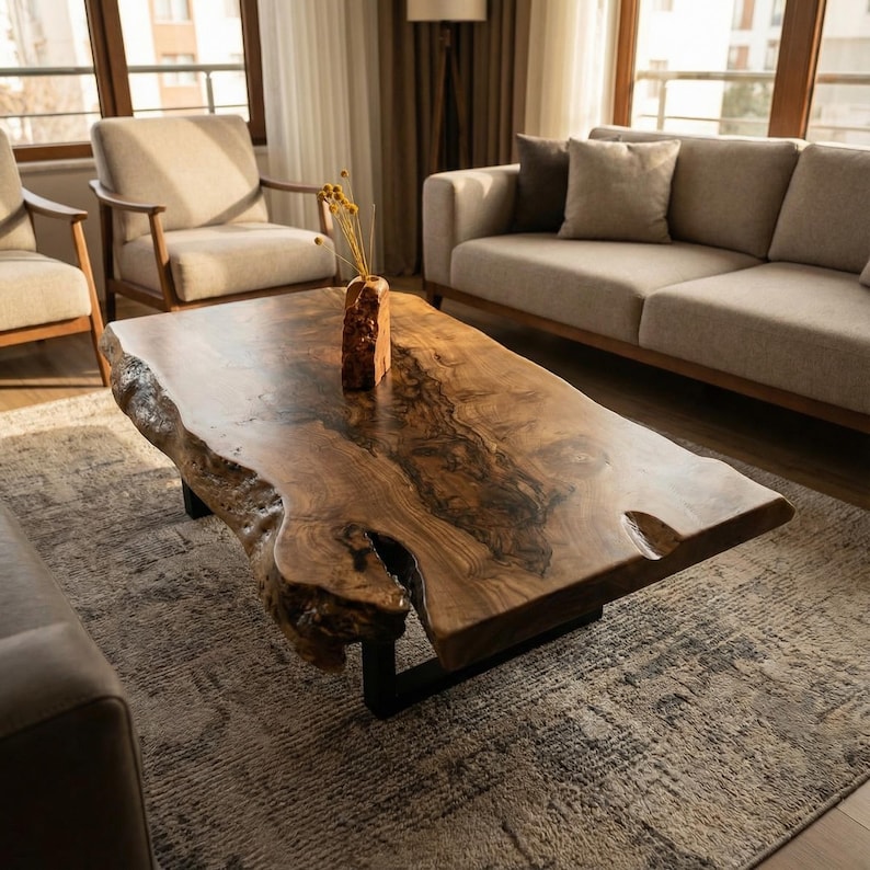 May include: A large, live-edge wooden coffee table with a natural, organic shape. The table is made of a rich, dark brown wood with unique grain patterns and sits on a black metal base. A decorative vase with dried flowers is on the table.