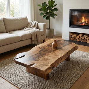 May include: A natural wood coffee table with a live edge design. The table has a rectangular shape and sits on a wooden base. A small, wooden vase sits on the table. The table is on a neutral-colored rug.