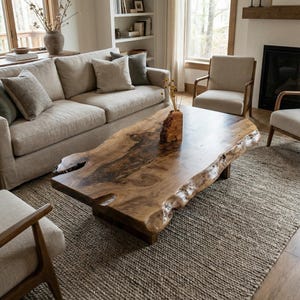 May include: A large, natural-edge wooden coffee table with a dark, polished surface. The table sits on a low, dark base and is the focal point of a living room with a neutral color palette. A woven rug and beige sofa complete the scene.