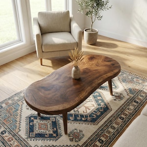 Könnte beinhalten: Ein dunkelbrauner, ovaler Couchtisch mit natürlicher Holzmaserung. Der Tisch wird von vier konischen Beinen getragen. Eine kleine Vase mit Weizenähren steht auf dem Tisch. Der Tisch steht auf einem gemusterten Teppich.