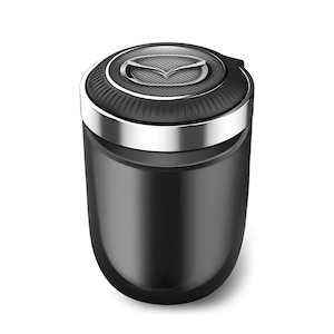 May include: A black car ashtray with a silver rim and a Mazda logo on the top. The ashtray is cylindrical with a glossy finish. The top has a ridged design around the logo.