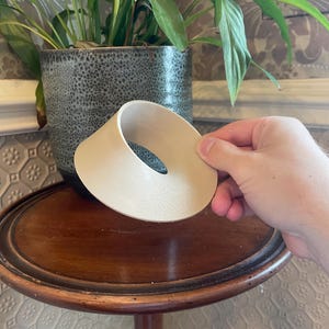 May include: A beige 3D printed Mobius strip object with a smooth, continuous surface and a single twisted loop design. The object is constructed from a light-colored material and features visible layer lines from the printing process throughout.