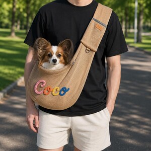 Puede incluir: Un transport&iacute;n de malla color canela para mascotas que se lleva cruzado sobre el pecho, con el nombre Coco bordado en hilo rosa, naranja, amarillo y azul. Un perro Papillon peque&ntilde;o de pelaje marr&oacute;n y blanco descansa dentro del bolso.