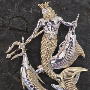 以下が含まれることがあります： 三叉の槍、王冠、魚の尾を持つ海の神を描いた、ツートンカラーの金属製ブローチ。神は三叉の槍を持ち、2匹の魚に挟まれています。ブローチは金と銀の色調で、暗い背景に配置されています。