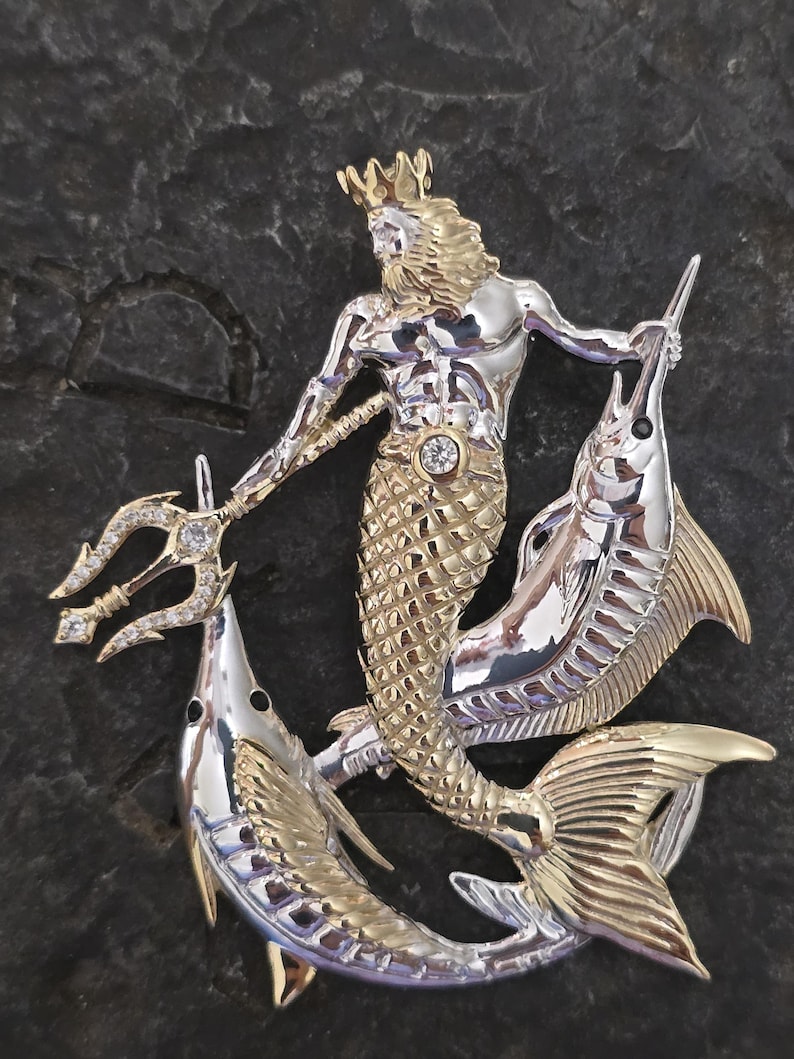 以下が含まれることがあります： 三叉の槍、王冠、魚の尾を持つ海の神を描いた、ツートンカラーの金属製ブローチ。神は三叉の槍を持ち、2匹の魚に挟まれています。ブローチは金と銀の色調で、暗い背景に配置されています。