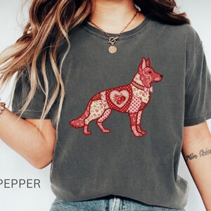 Puede incluir: Camiseta gris oscuro con un diseño de pastor alemán en patchwork con patrones florales y de corazón en tonos rojos y rosas. La palabra "PEPPER" está impresa en la parte inferior de la imagen.