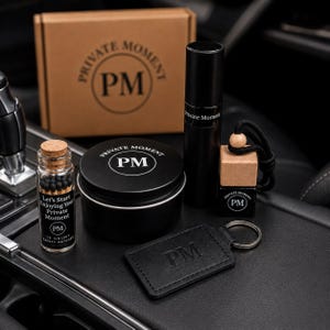 May include: A gift set featuring a brown cardboard box, a glass bottle with 18 black-tipped matches, a black metal tin, a black cylindrical spray bottle, a small square glass bottle with a wooden cap and black cord, and a black leather keychain, all labeled PM.