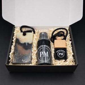May include: A gift box containing a rectangular black and cream resin air freshener with gold flakes, a clear spray bottle labeled Private Moment PM, and a small black glass bottle with a wooden cap and black cord labeled Private Moment PM.