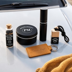 May include: A set containing a glass bottle of matches with a label reading Let's Start Enjoying Your Private Moment, a black tin with a PM logo, a black cylindrical spray bottle, a black car air freshener with a PM logo, and a tan leather keychain.