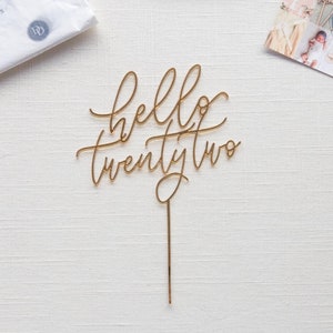 May include: Gold cake topper with the words "hello twenty two" in a cursive font.
