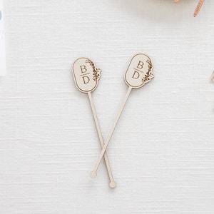 May include: Two wooden cocktail stirrers with a floral design and the initials "B & D" engraved on the top.