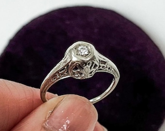 May include: A delicate silver ring with a single, round diamond set in a filigree design.
