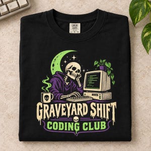 May include: A black t-shirt featuring a graphic of a skeleton in a purple hoodie typing on a computer. The design includes a crescent moon, a steaming mug with a skull, a potted plant, and the text "GRAVEYARD SHIFT CODING CLUB" in a dripping font.