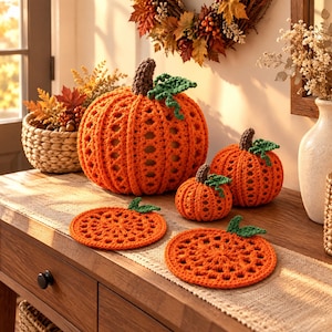 Peut inclure: Trois citrouilles crochetées orange de tailles variées et deux dessous de verre plats en forme de citrouille orange. Chaque citrouille présente une tige marron foncé et des feuilles vertes. Les articles sont réalisés avec un point ajouré.