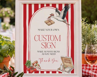 May include: A framed sign with red and white stripes and the text "MAKE YOUR OWN CUSTOM SIGN". The sign features a stork carrying a package, pizza, and a special delivery box. The sign is on a wooden table with plants and a glass of wine.