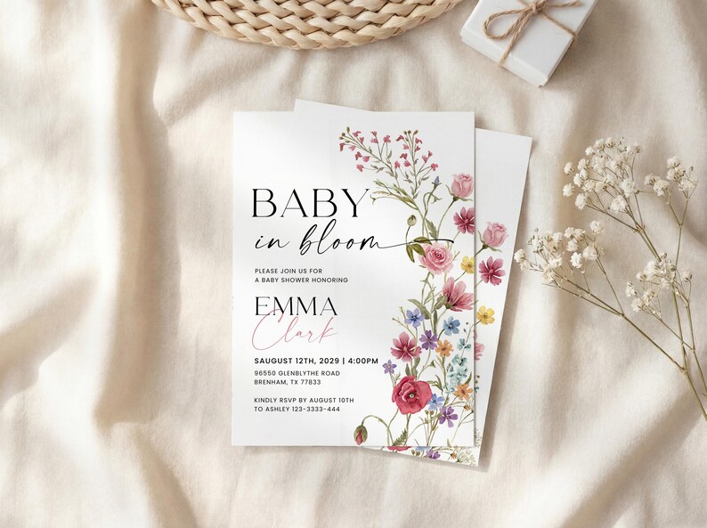May include: Baby shower invitation with floral design. The invitation reads "Baby in Bloom" with the name "Emma Clark" and event details. The design features a watercolor floral border with pink, red, and purple flowers.