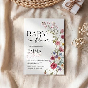 May include: A baby shower invitation with the text "BABY in bloom" and the name "EMMA Clark". The invitation is decorated with a floral design in pink, red, and purple. The invitation also includes the date, time, and location of the baby shower.