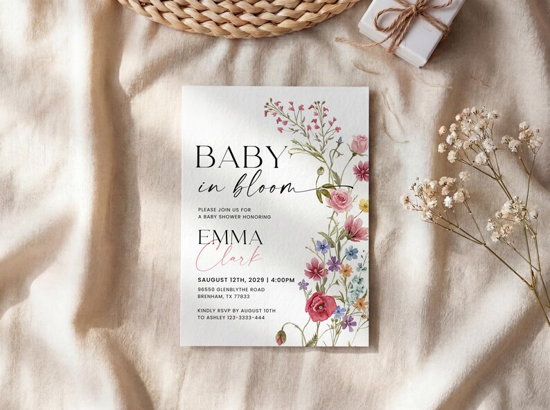 May include: A baby shower invitation with the text "BABY in bloom" and the name "EMMA Clark". The invitation is decorated with a floral design in pink, red, and purple. The invitation also includes the date, time, and location of the baby shower.