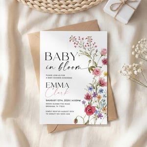 May include: A baby shower invitation with the text "Baby in Bloom" and the name "Emma Clark". The invitation features floral illustrations in pink, red, and purple hues. The invitation is on a white background.