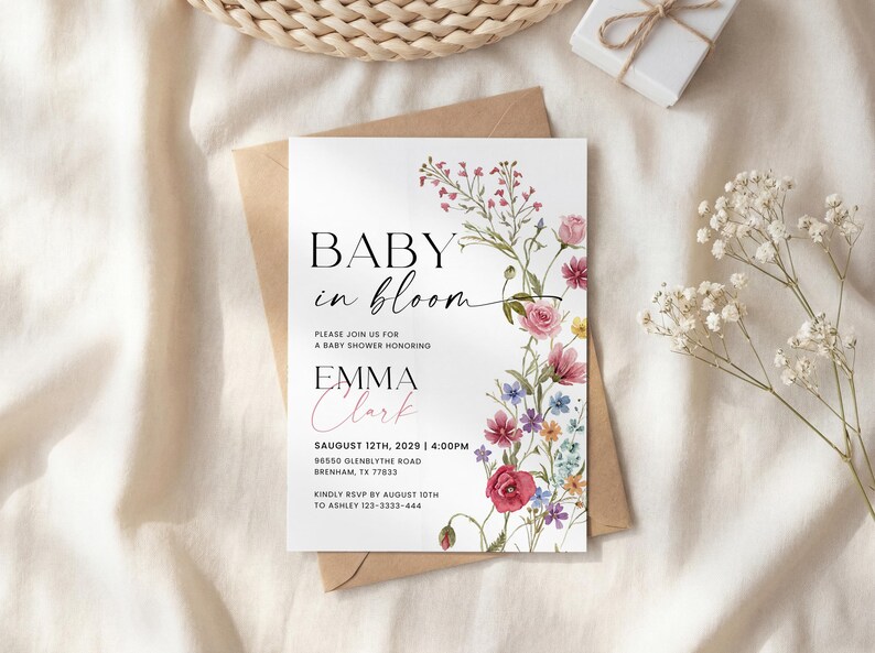 May include: A baby shower invitation with the text "Baby in Bloom" and the name "Emma Clark". The invitation features floral illustrations in pink, red, and purple hues. The invitation is on a white background.