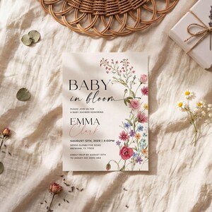 May include: A baby shower invitation with the text "BABY in bloom" and floral illustrations. The invitation includes the name "EMMA Clark" and event details. The invitation is on a cream-colored background with decorative elements.