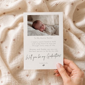 Może przedstawiać: Prostokątna biała karta ze zdjęciem śpiącego niemowlęcia u góry. Tekst brzmi: To My Auntie Rachel, I need a warm hand to hold and a big heart to love me through every step of life. Mummy and Daddy say you are the best person to be by my side. Will you be my Godmother? Love Lily, z małą ikoną odcisku stopy.