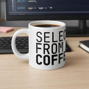 Puede incluir: Taza de café de cerámica blanca llena de café oscuro. La taza tiene el texto "SELECT FROM COFFEE" impreso en letras negras grandes y en negrita. La taza está sobre una superficie de madera clara.