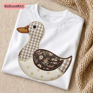 Peut inclure: T-shirt blanc avec un motif de canard appliqué. Le canard a un corps à carreaux marron et blanc, une aile florale et un ventre beige à pois. Le texte "BizBrandKit" est dans le coin supérieur gauche.