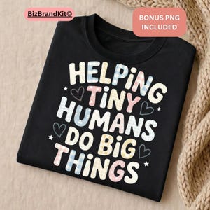 Puede incluir: Camiseta negra con el texto "HELPING TINY HUMANS DO BIG THINGS" en letras blancas, azules, rosas y amarillas. Las palabras están decoradas con corazones y estrellas. La camiseta está doblada sobre una superficie beige.