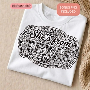 May include: White t-shirt featuring a brown decorative design with the text "She's from TEXAS". The design is in a western style with intricate details and a rope-like border. The shirt is folded and ready to wear.
