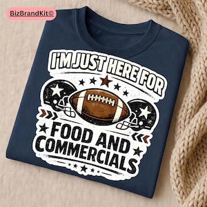 Op de afbeelding: Marineblauw t-shirt met een voetbalontwerp en de tekst "I'M JUST HERE FOR FOOD AND COMMERCIALS". Het ontwerp bevat een voetbal, helmen en sterren.