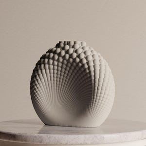 Może przedstawiać: Matowy, kremowobiały wazon ceramiczny o kulistym kształcie i teksturowanej powierzchni, z gęstym wzorem małych, wypukłych okrągłych guzków, które promieniują na zewnątrz w spiralnym układzie, tworząc wyraźny efekt trójwymiarowy.