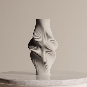 May include: A matte off-white vase featuring a complex, vertically ribbed surface with a distinct twisted, hourglass-like silhouette. The object has a narrow neck and base that expands into two symmetrical, undulating curves along its central body.